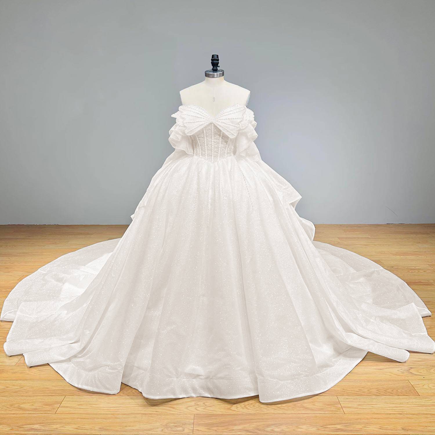 Full-length studio front shot of the complete luxury pearl-and-sparkle bridal ball gown on a mannequin against a neutral gray background.
