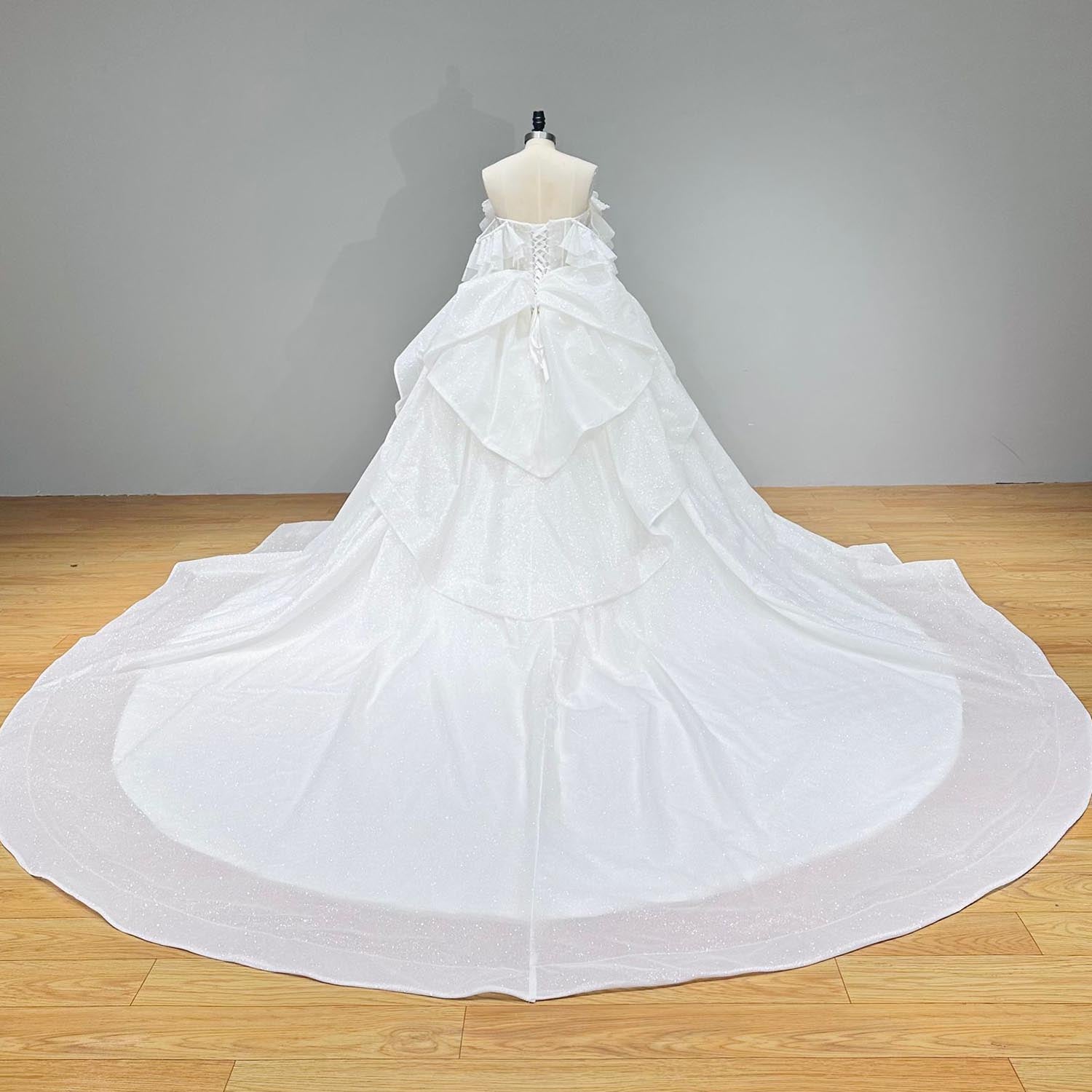 Studio back view of a glitter ball gown wedding dress on a mannequin, highlighting the classic lace-up corset tie and multi-layered cascading bustle train.