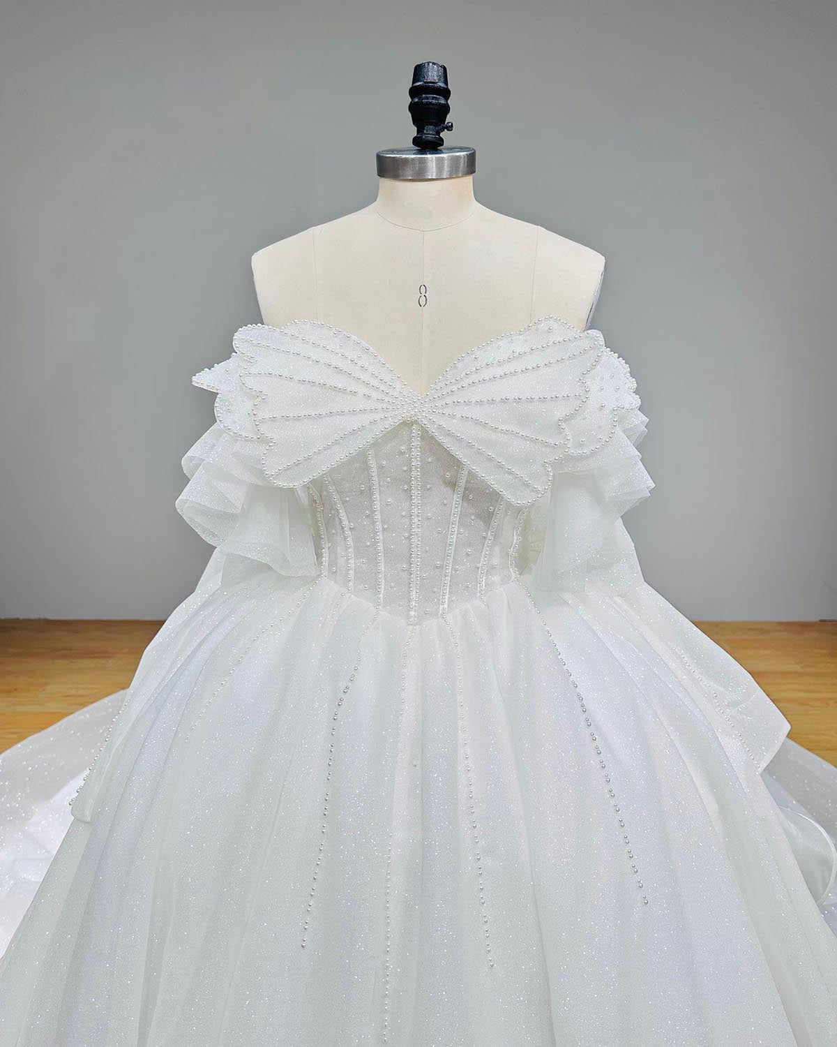 Macro detail of a structured bridal corset bodice heavily encrusted with vertical rows of white seed pearls and delicate crystals beneath a pleated mesh bow collar.