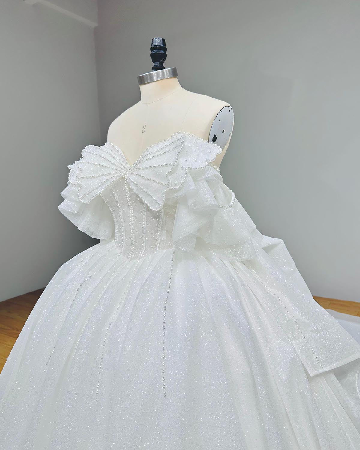 Side angle profile of an off-the-shoulder couture wedding gown bodice, showing the fine tailoring of the sheer boned corset and tiered ruffle sleeves on a mannequin.