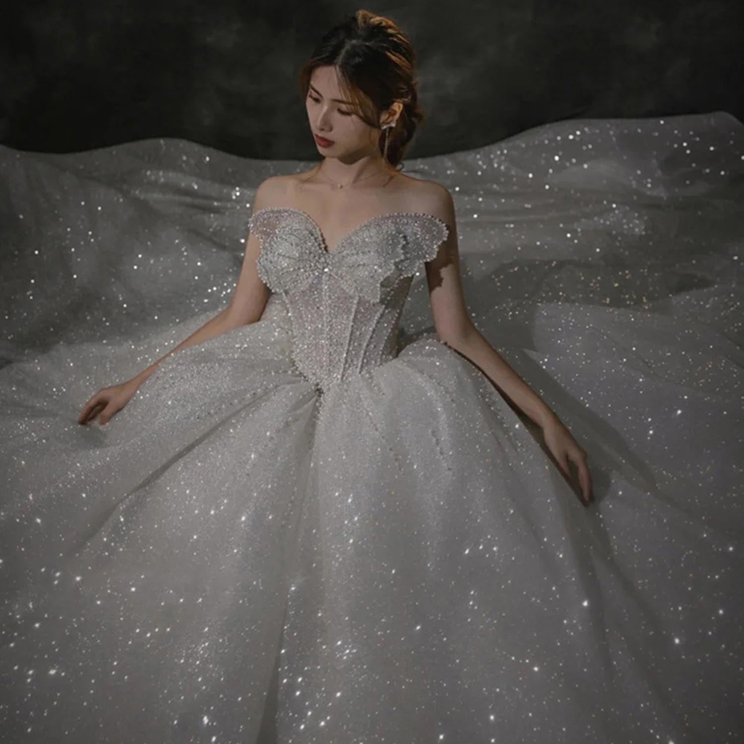 Dramatic low-light portrait of a model sitting in a heavily textured diamond-glitter wedding dress that reflects light across a expansive princess skirt.