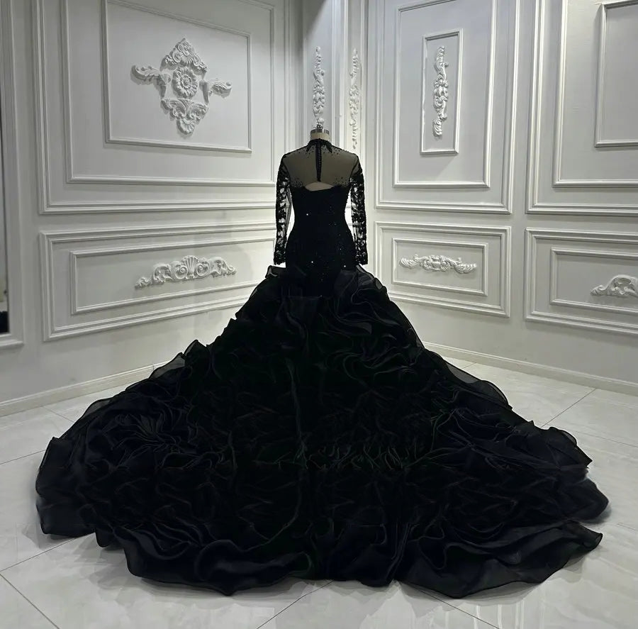 Rear view of the black bridal gown on a mannequin, showcasing a sheer illusion lace back with corset-style ribbon lacing and an expansive, multi-layered ruffled mermaid train.