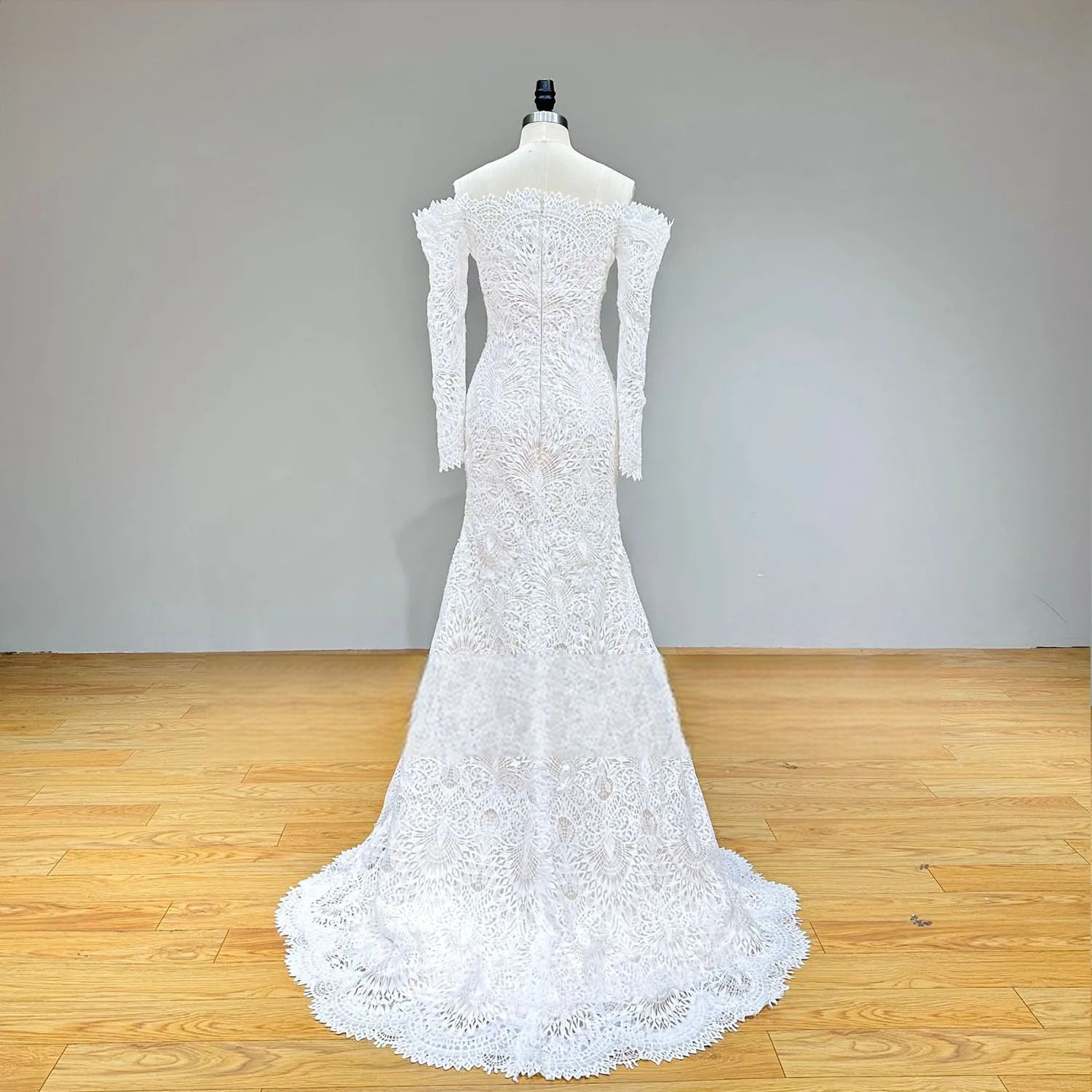 Rear perspective of a mermaid-style wedding gown with long sleeves, illustrating the seamless zipper back closure and the sweeping scalloped lace train.