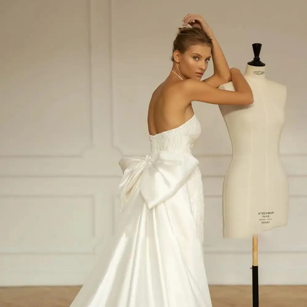 Rear view of a lace-embroidered trumpet bridal gown on a mannequin showcasing a majestic detachable satin overskirt with a prominent statement back bow.