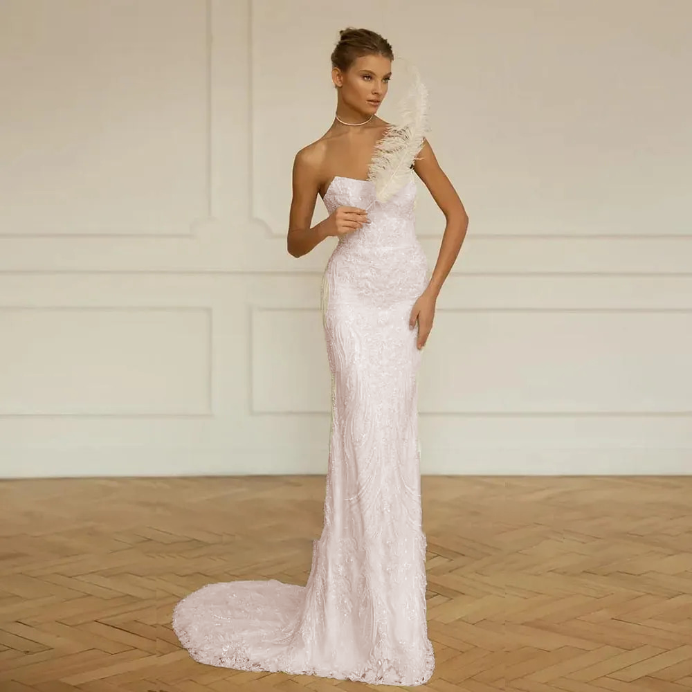 Romantic soft blush pink mermaid wedding gown featuring an all-over white sequin leaf lace pattern, a strapless sweetheart cut, and a flowing trumpet train.