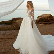 Bohemian V-neck mermaid wedding dress with long lace sleeves and a detachable train, photographed on a scenic beach.