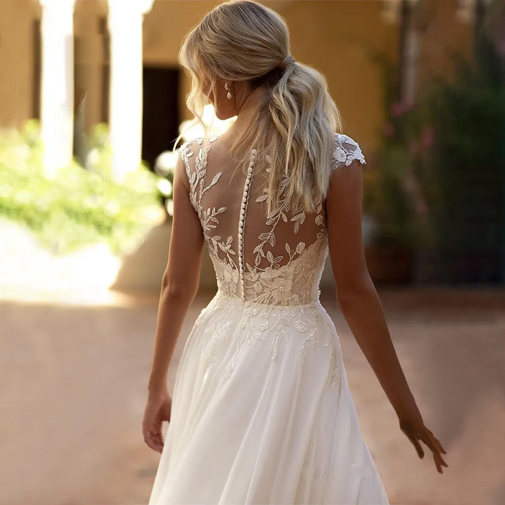 Rear profile of an elegant boho lace bridal dress with a button-up illusion back and flowing chiffon A-line skirt.