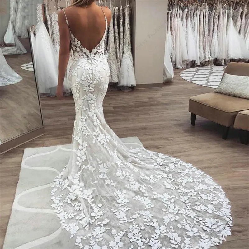 Full-length back view of a bohemian mermaid bridal gown featuring elaborate floral lace appliqué, spaghetti straps, and a sweeping train.