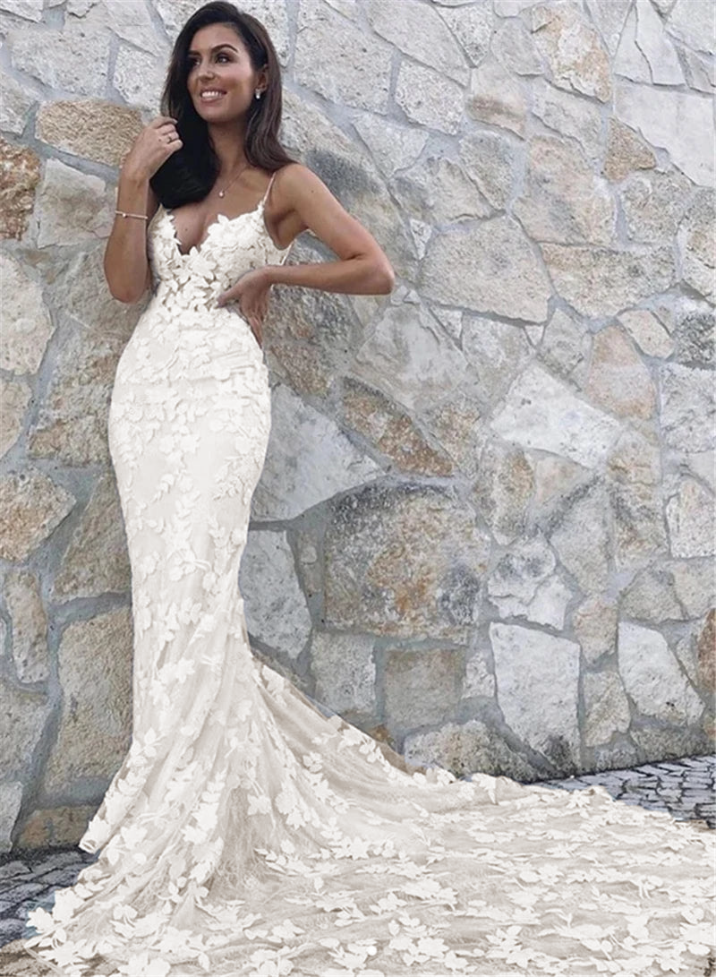 A full-length portrait of a bride wearing a boho lace appliqué mermaid wedding gown with a dramatic, detailed train.