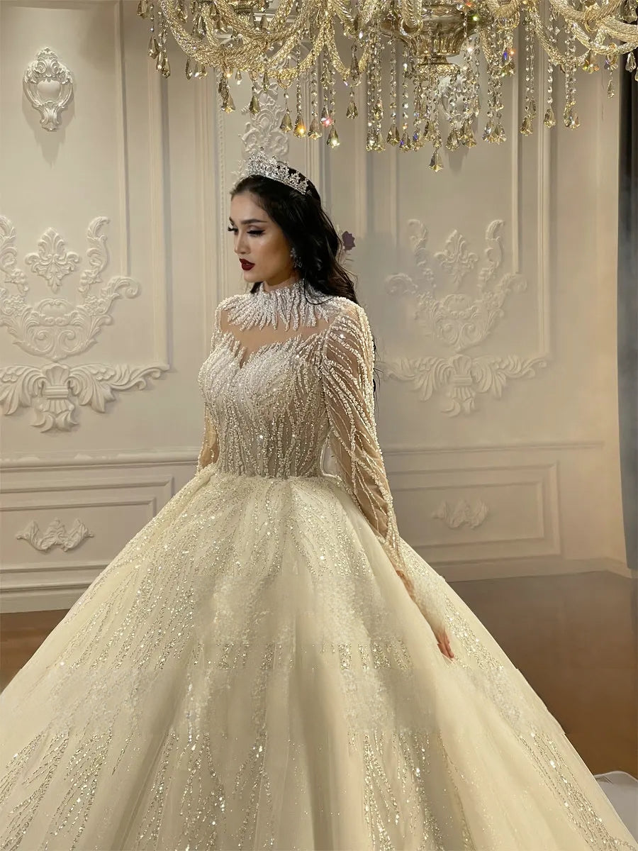 Close-up side profile of an elegant bridal gown with a high-neck fringe collar, sheer beaded long sleeves, and a matching royal crystal tiara.