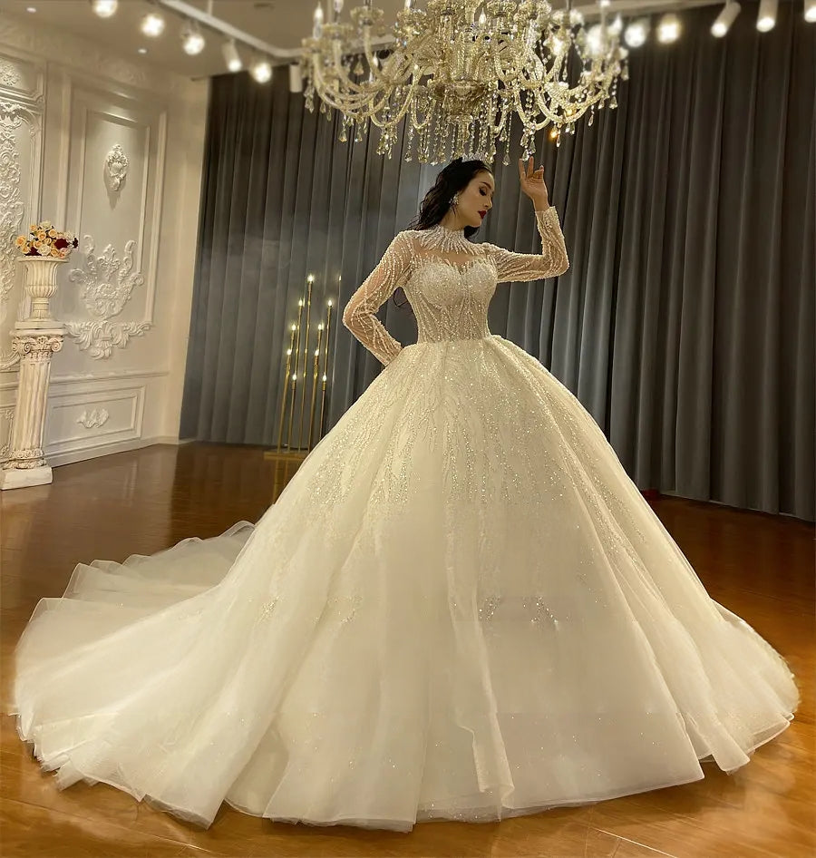 Full-length angled view of a long sleeve bridal wear ball gown with a massive layered tulle skirt and sparkling finish, reflecting a regal and classic wedding style.
