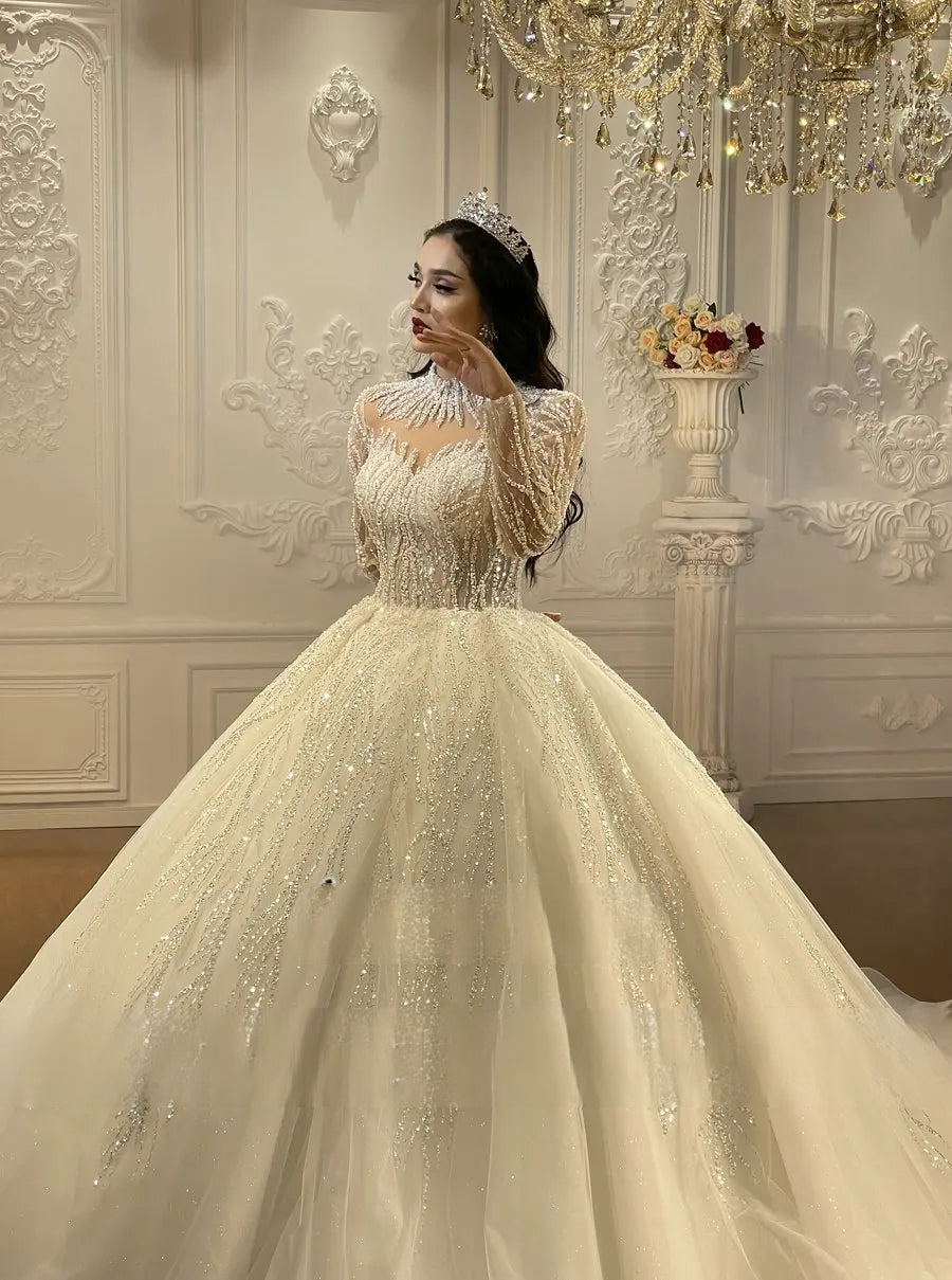 Side-angle portrait of an elegant long sleeve bridal dress showcasing the high-quality silver embroidery and the voluminous sweep of the cathedral-length ballroom skirt.