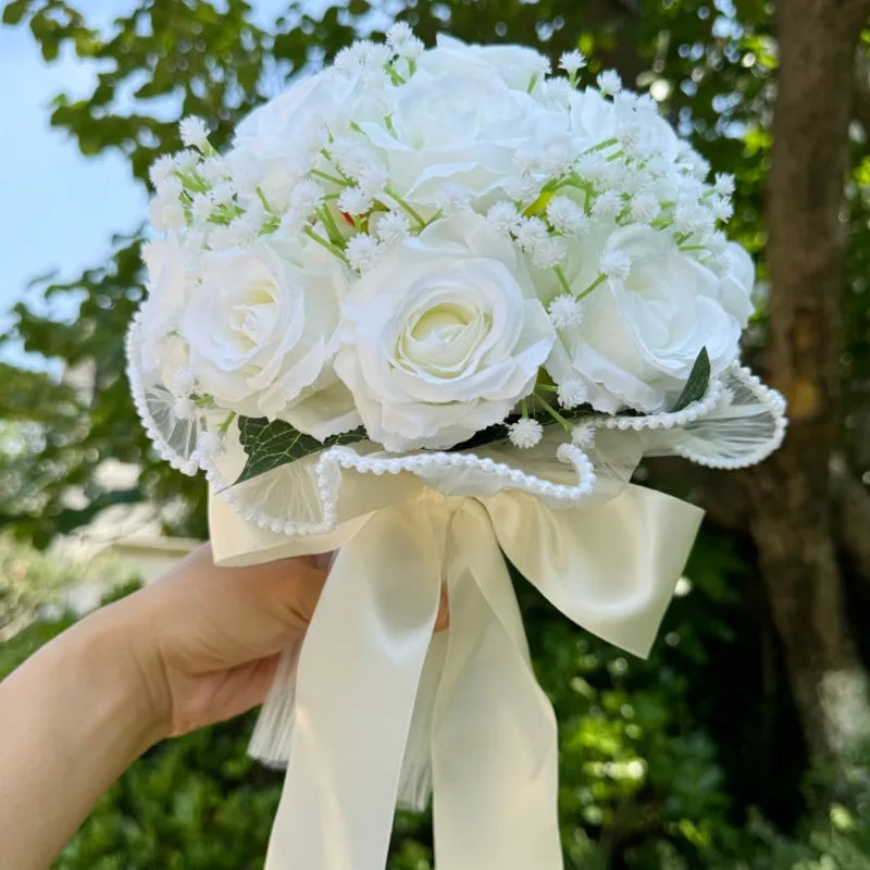 Low-angle shot of a handmade white silk rose bridesmaid bouquet showing the elegant satin handle wrap and wide satin ribbon bow.