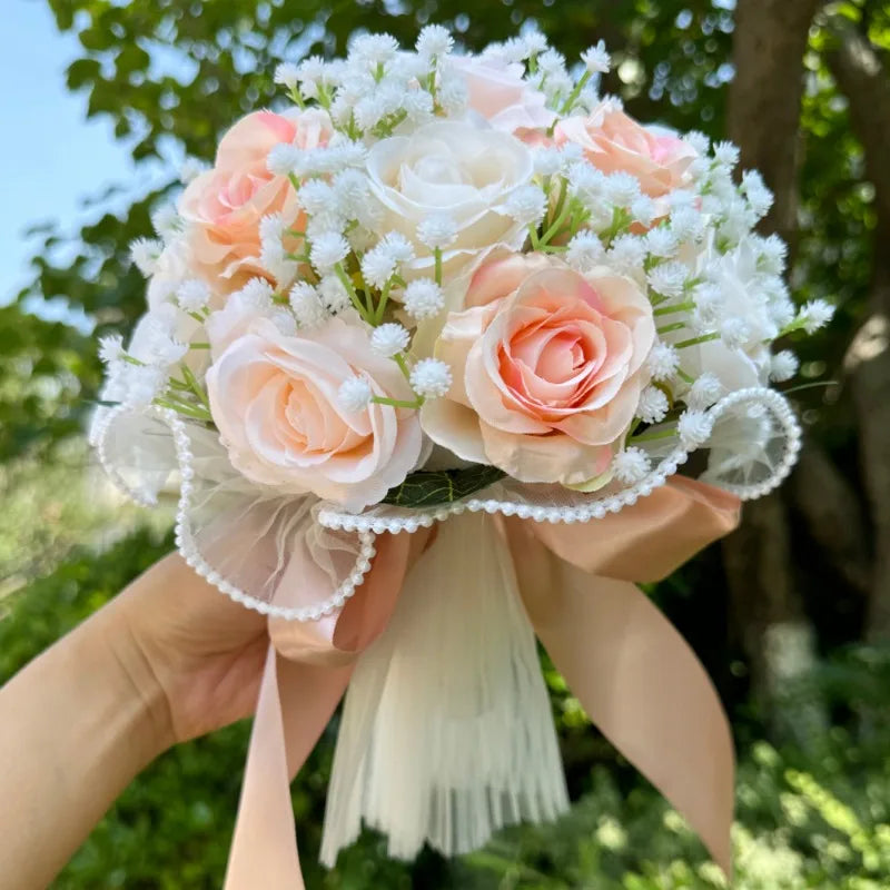 Handheld artificial bridesmaid bouquet featuring delicate champagne and blush pink silk roses accented with white floral sprigs.