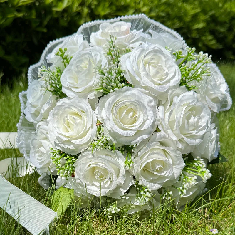 Close-up top view of a handmade pure white silk rose wedding bouquet accented with small green filler sprigs and a delicate pearl-trimmed lace border.