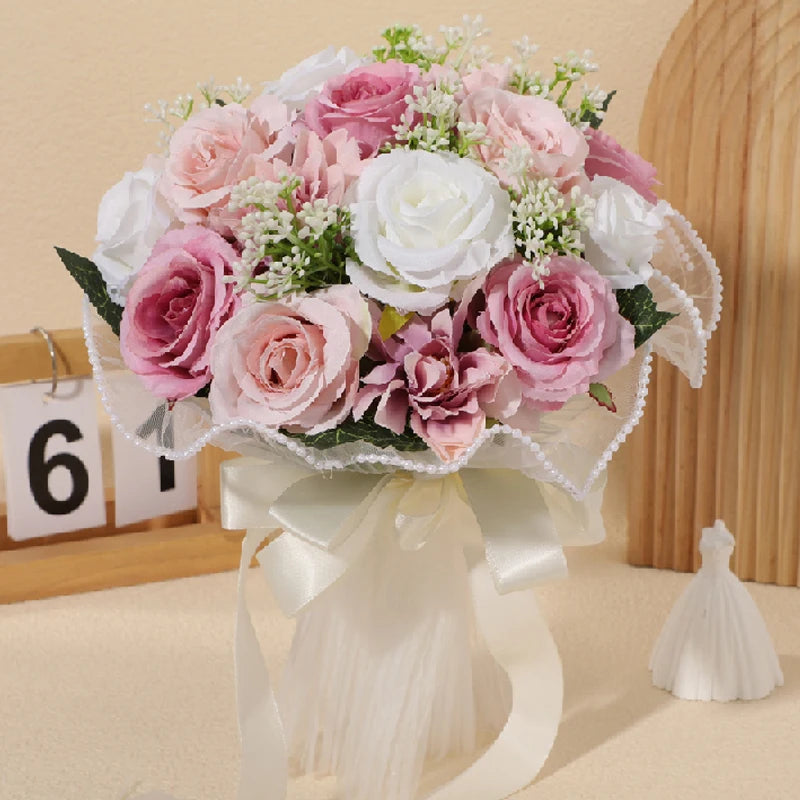 Front display of a rustic pink, mauve, and white silk rose bridesmaid bouquet adorned with baby's breath, a sheer pearl-beaded lace collar, and a wide cream satin ribbon bow.