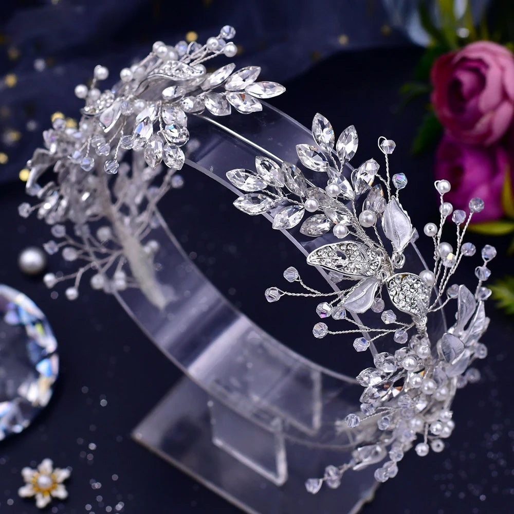 High-angle macro shot of a clear silver crystal bridal headband with marquise-cut rhinestones and silver leaf accents displayed on an acrylic stand.