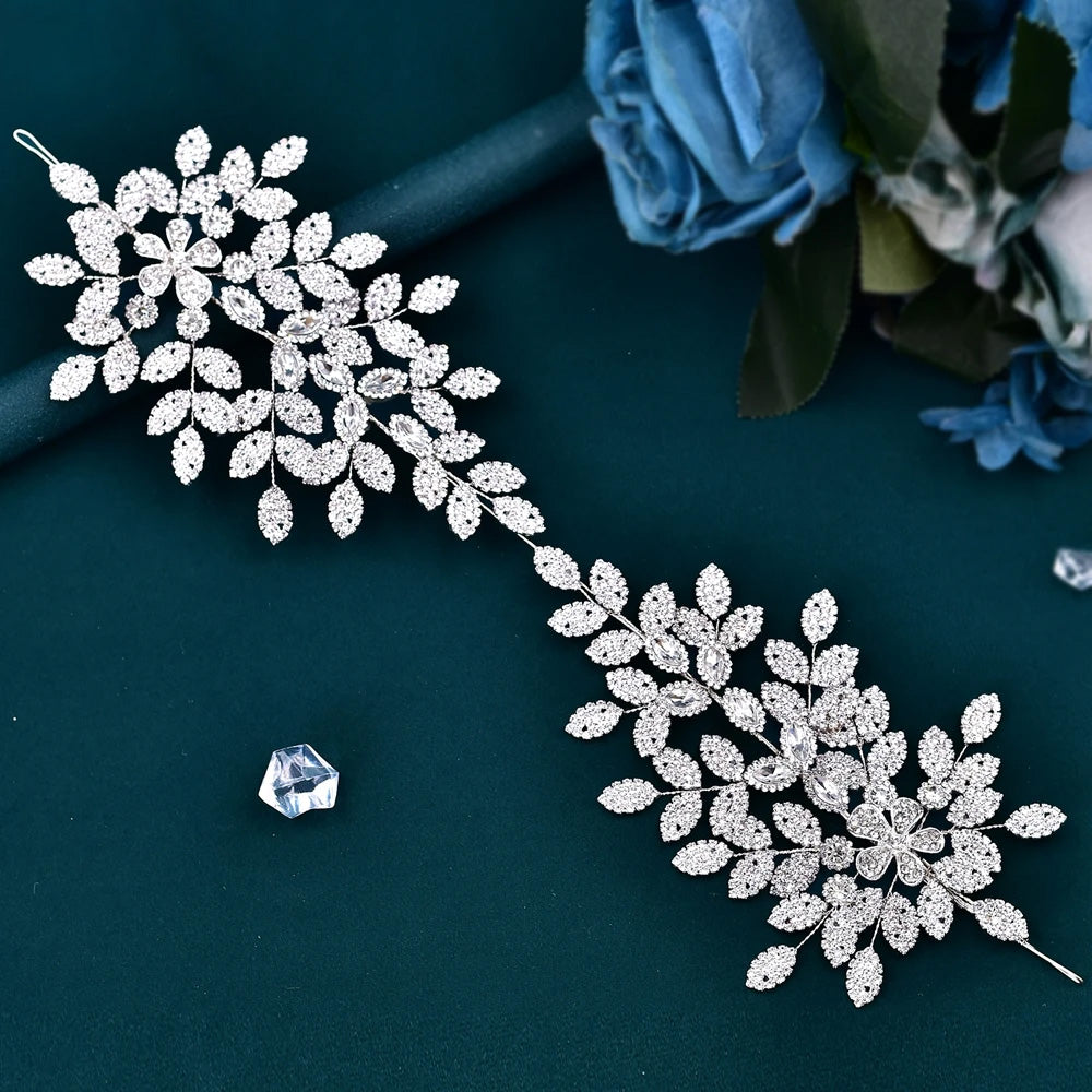 Flat lay view of a flexible silver crystal bridal hair vine accessory with pavé rhinestone leaf clusters over a dark teal background.