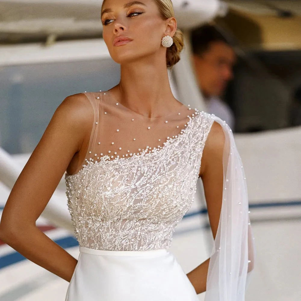 Close-up of a bridal gown featuring a sheer illusion neckline adorned with pearls and intricate beadwork on a sleeveless bodice.