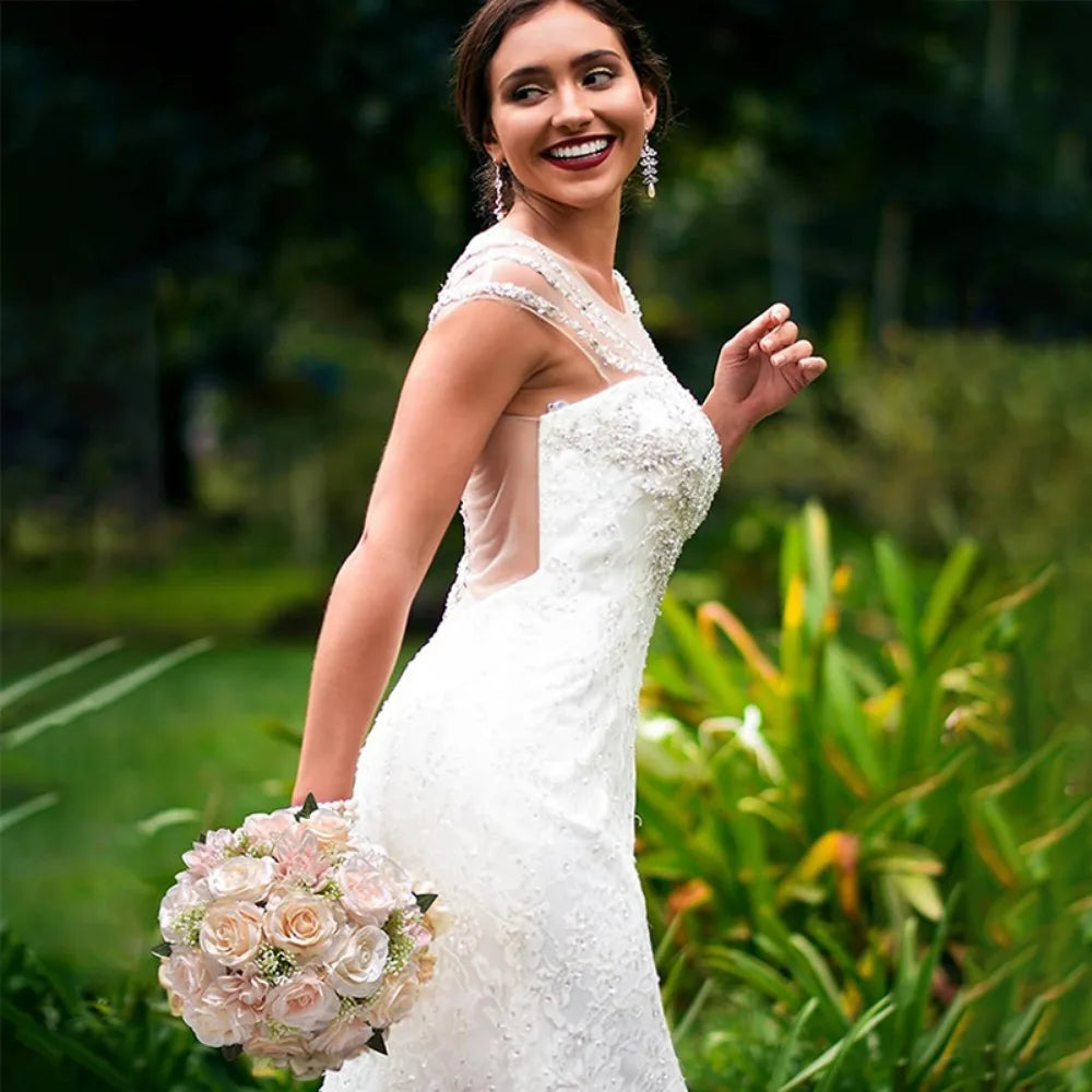 A bride in a lace gown looking over her shoulder while carrying a pastel pink and cream handmade artificial wedding bouquet.