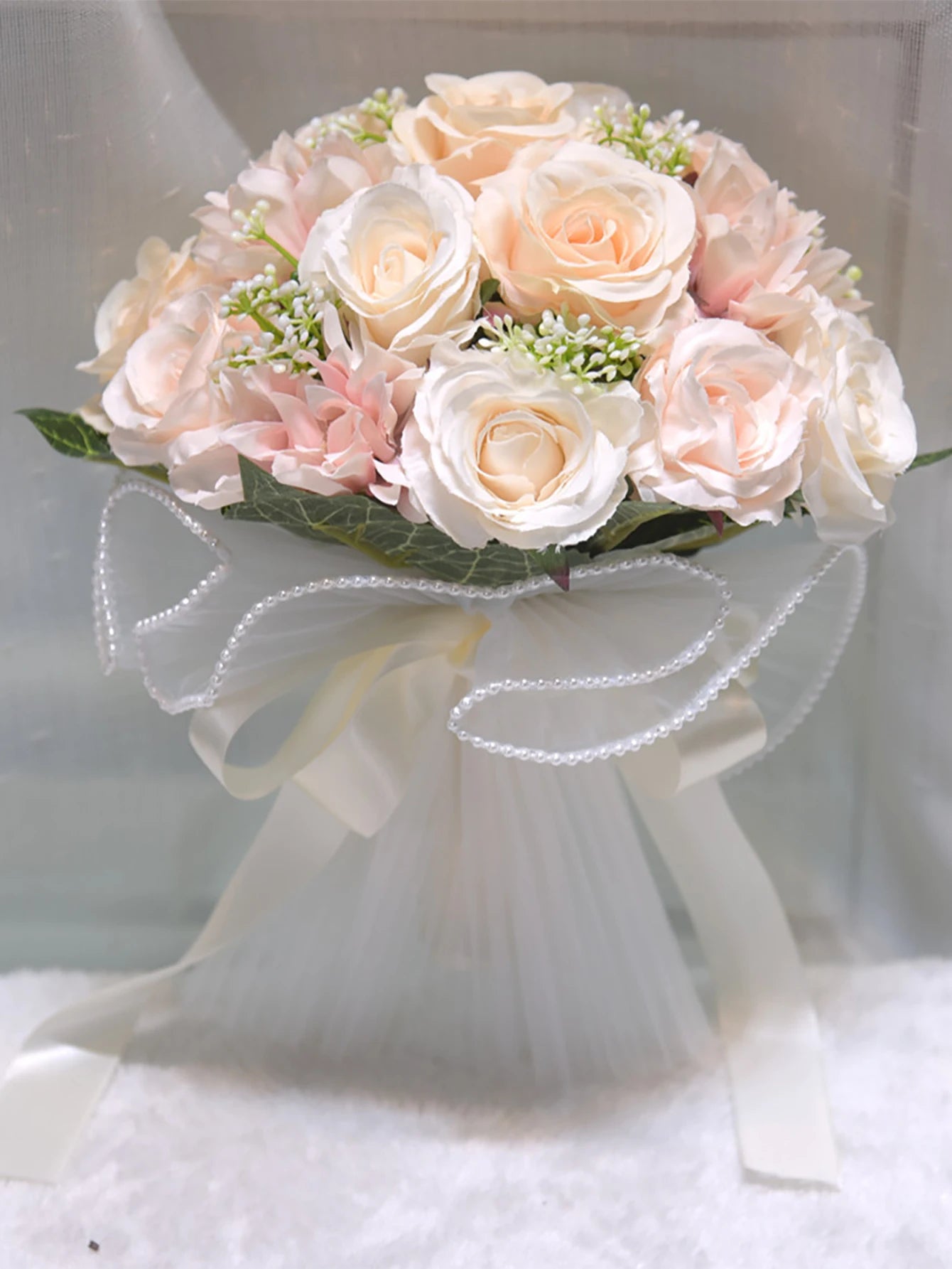 A peach and champagne artificial wedding flower arrangement wrapped in white tulle and detailed with a decorative pearl wire loop bow.