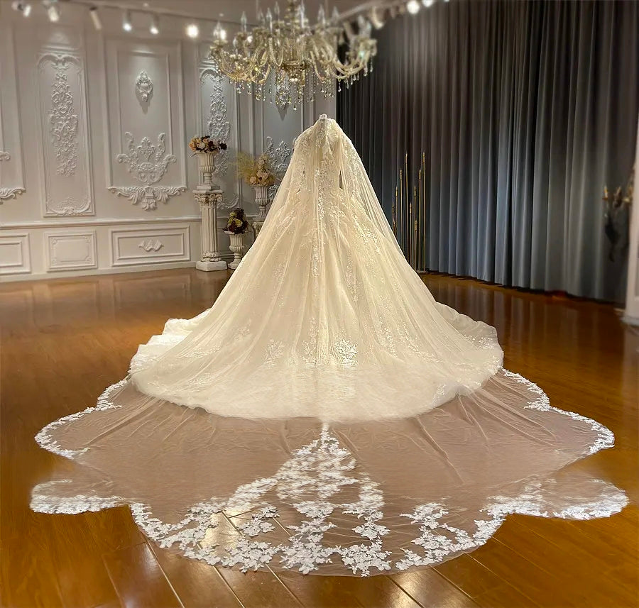 Breathtaking rear view of a luxury wedding dress featuring a massive cathedral train with lace-trimmed edges and a full-length sheer veil cascading over a ballroom floor.