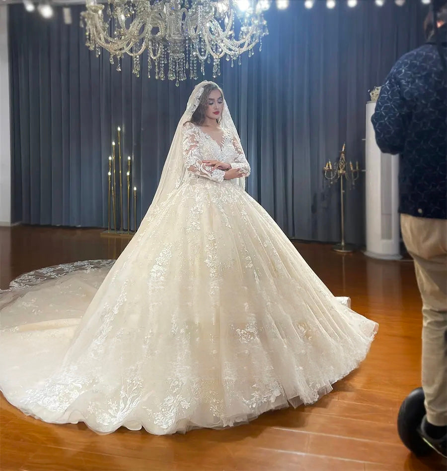 Side profile of a model in a luxury champagne long-sleeved wedding dress, emphasizing the regal ball gown silhouette and the delicate lace patterns on the sheer illusion bodice and sleeves.