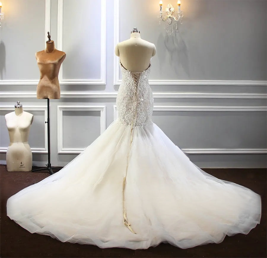 Rear view of the champagne mermaid wedding gown on a mannequin, displaying a traditional lace-up corset back and an expansive, shimmering tulle train.