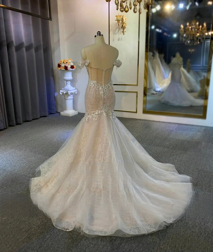 Back 3/4 view of a luxury champagne mermaid bridal gown highlighting the sheer corset back and flared lace train.