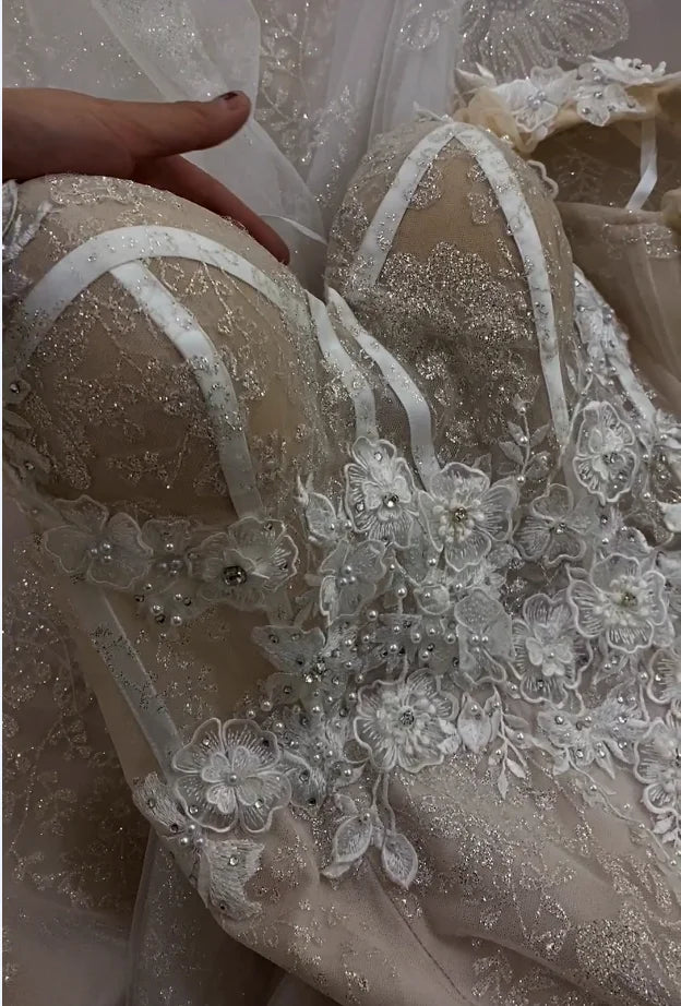 Macro shot of the sweetheart neckline featuring delicate pearl beads and 3D flower accents on a champagne bridal dress.