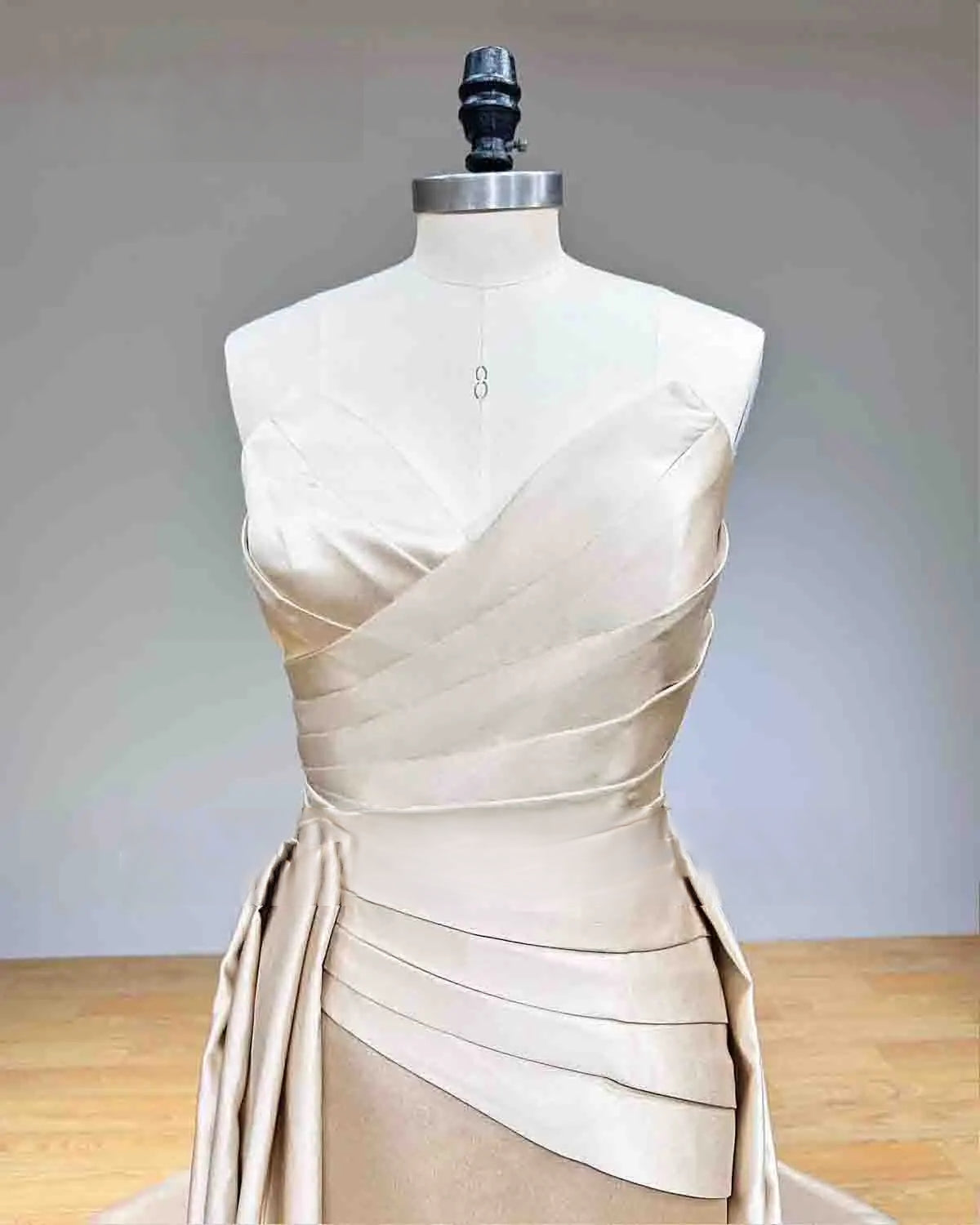 Close-up detail of the intricate pleated wrap bodice on a champagne satin wedding dress, showcasing the elegant sweetheart-inspired neckline.