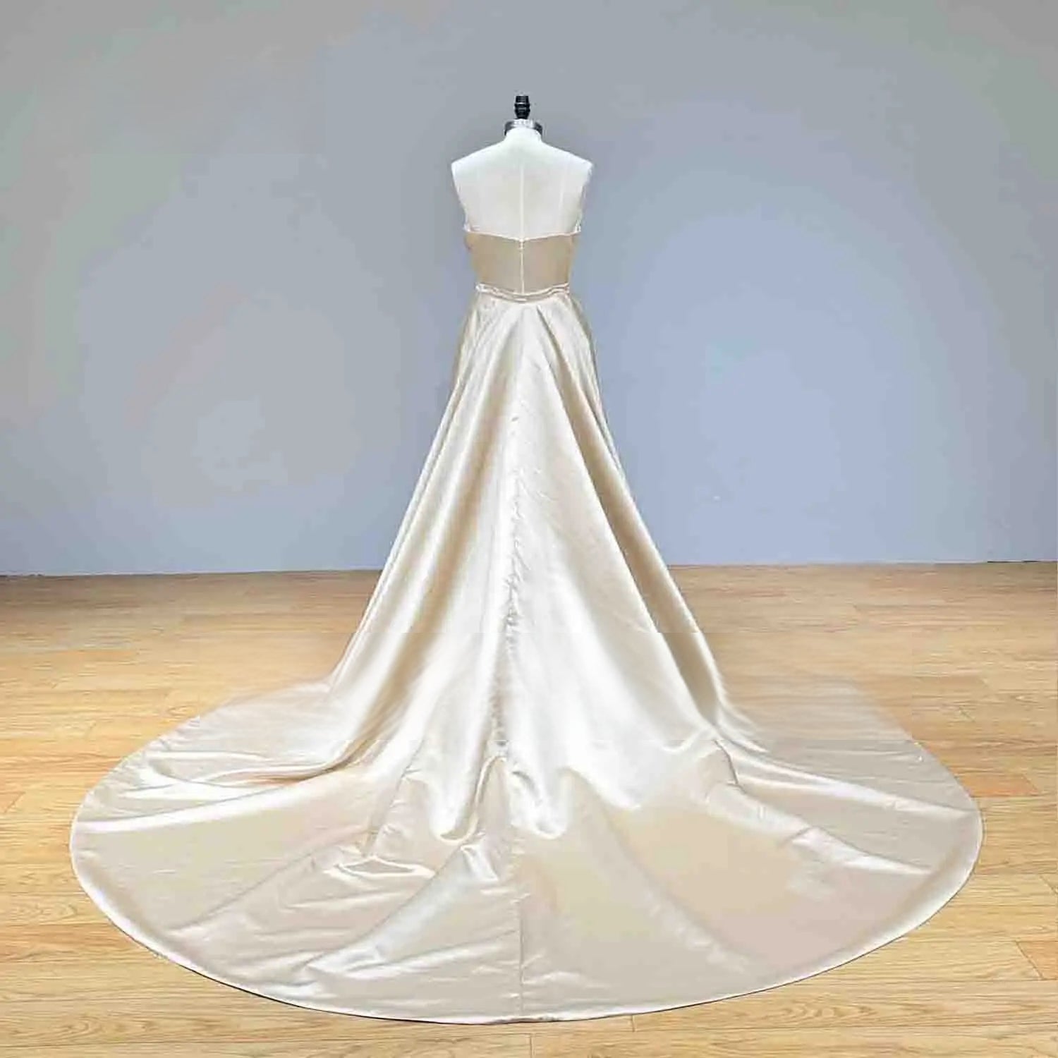 Rear perspective of a champagne satin mermaid wedding dress on a mannequin, highlighting the sleek back design and a sweeping circular train.