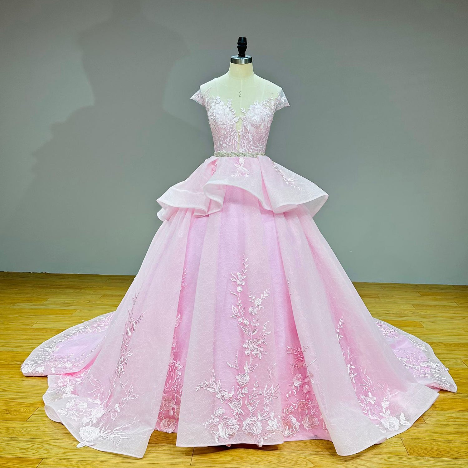 Full front studio product photography of the unique pink and white ball gown bridal dress with a tiered skirt and crystal beaded belt on a mannequin.