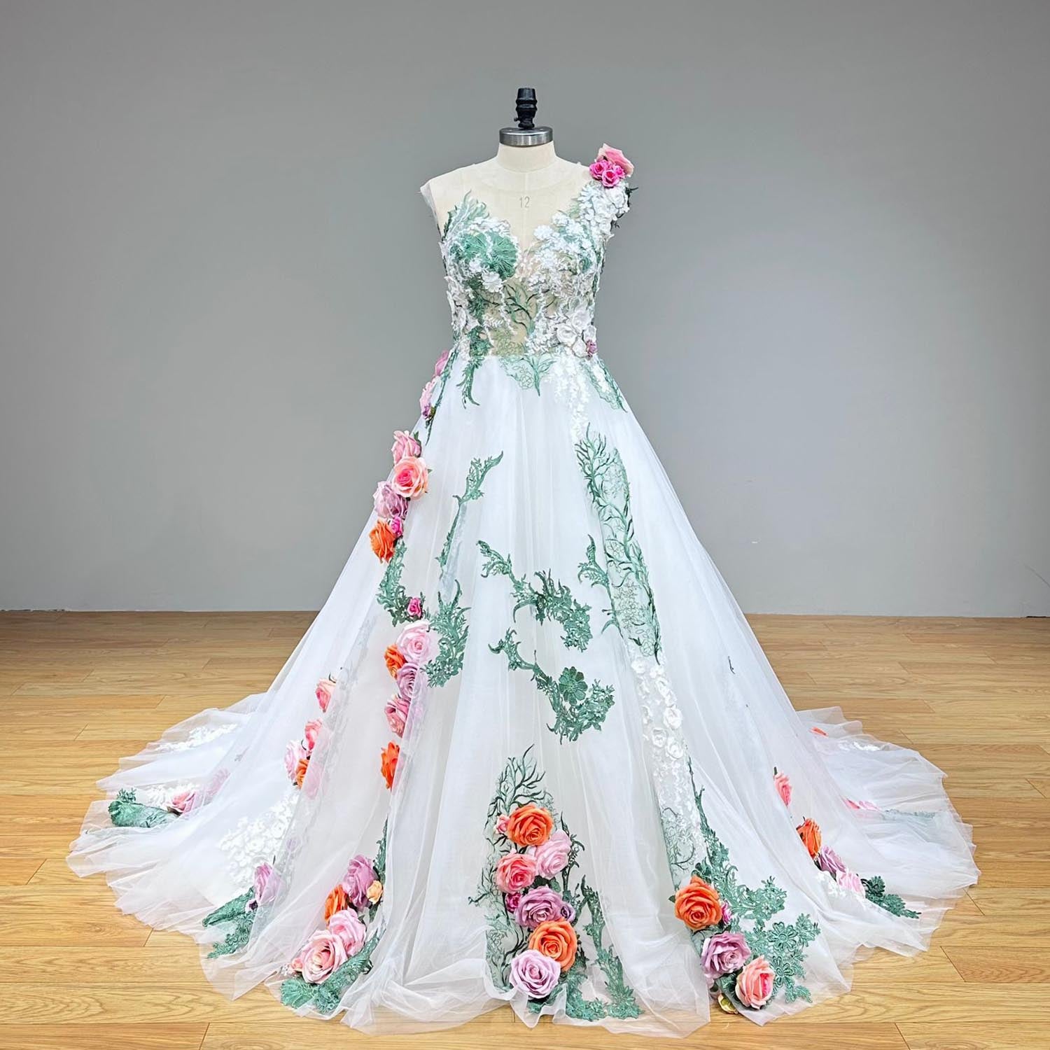 Studio front view of an off-the-shoulder colorful tulle ball gown wedding dress on a mannequin, emphasizing the green embroidered vines and striking 3D flowers cascading down the skirt.