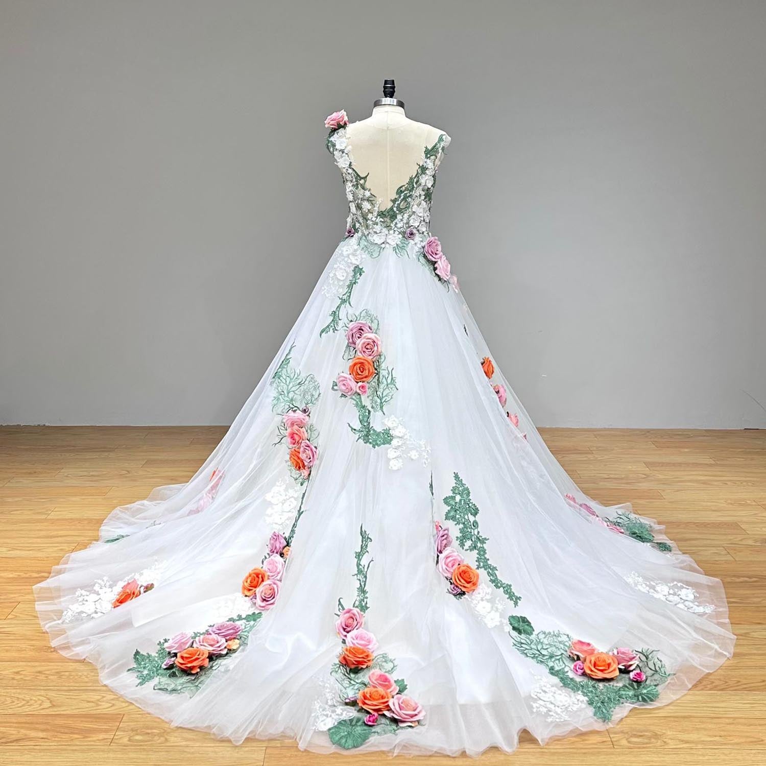 Dramatic full back view of an off-the-shoulder colorful tulle ball gown wedding dress on a mannequin, showcasing the sweeping tulle train heavily accented with green vine embroidery and colorful 3D flowers.