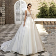 Elegant A-line satin wedding dress with a V-neckline and intricate lace bodice, featuring a dramatic train in a classic outdoor setting.