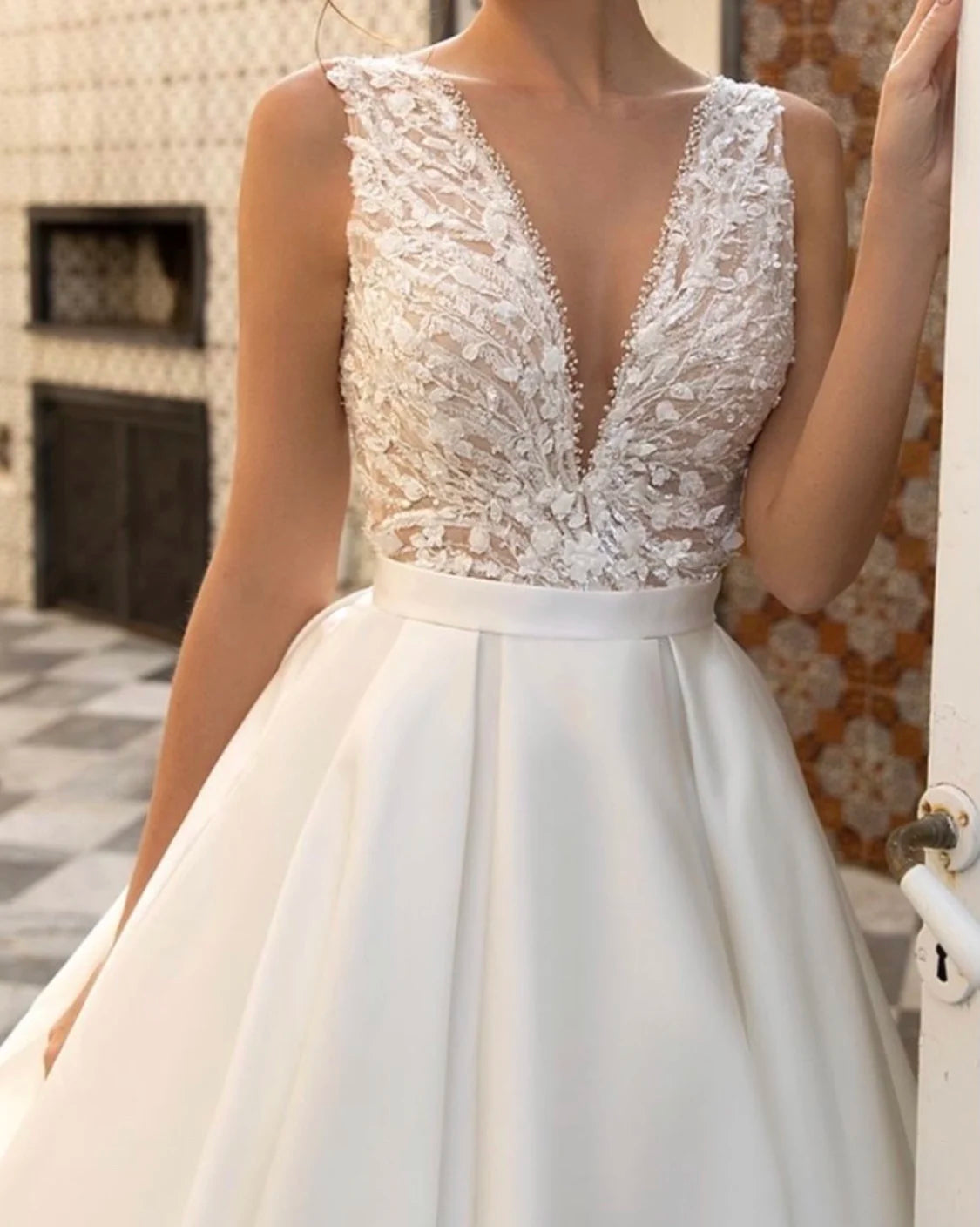 Close-up of a bridal gown bodice showcasing a deep V-neck, floral lace embroidery, and a smooth satin waistband.