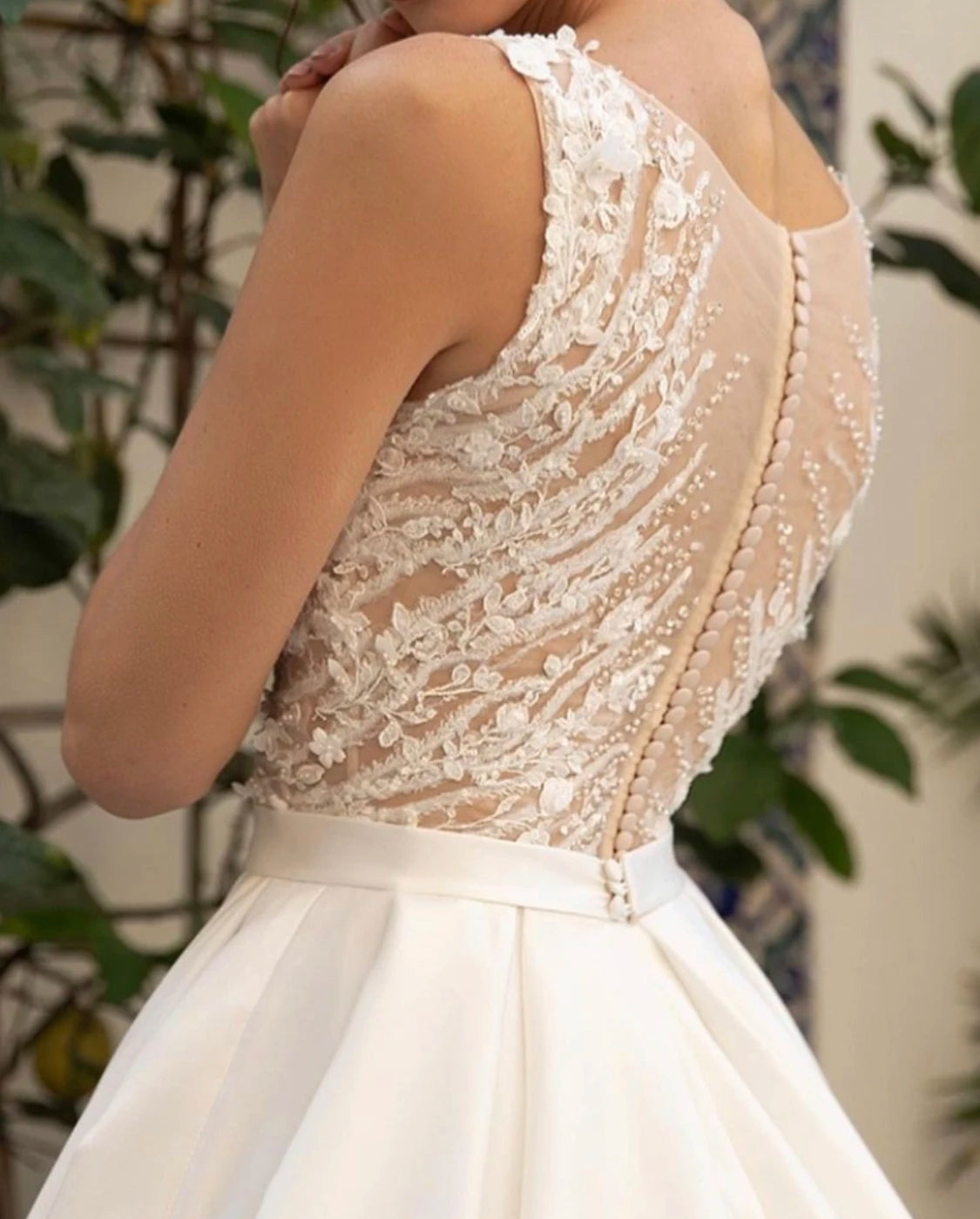Detail view of the back of a bridal gown featuring a sheer illusion back with delicate floral lace and a vertical row of elegant fabric buttons.
