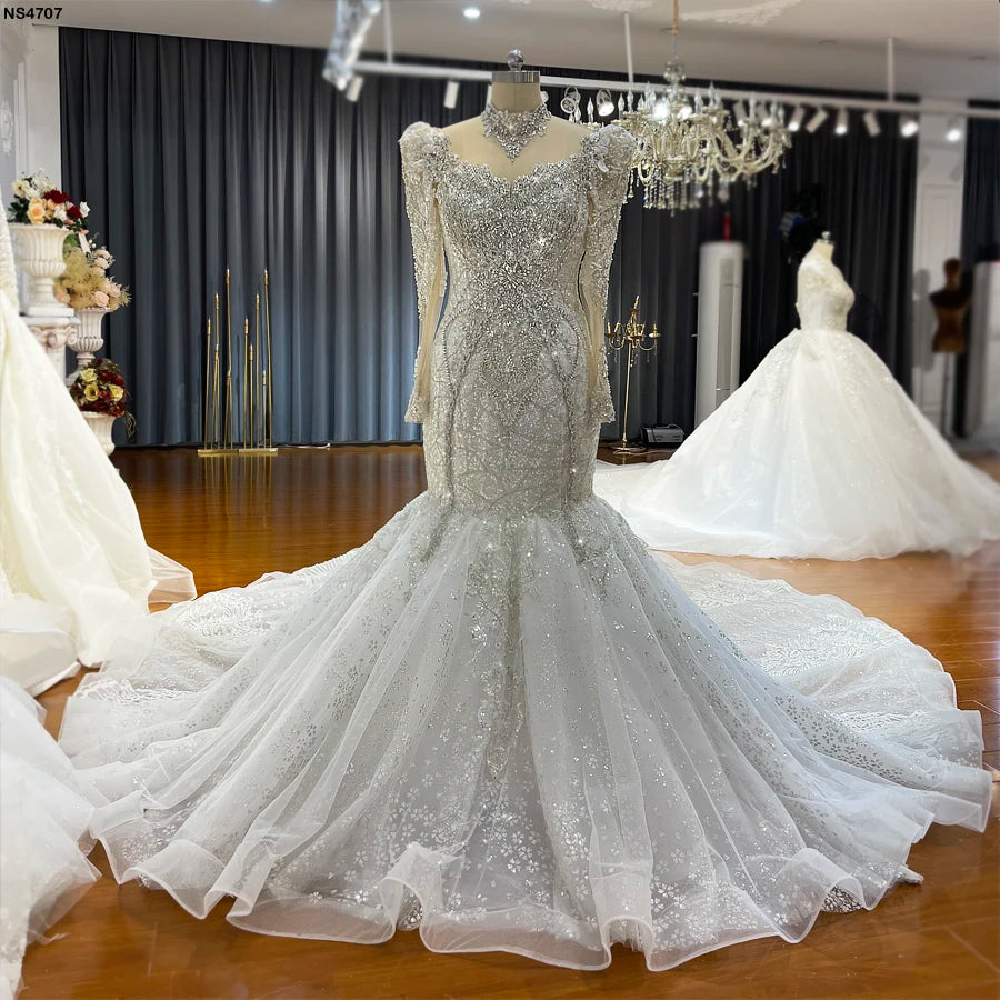 Front-facing shot of a crystal-embellished luxury mermaid wedding dress displayed on a mannequin, showcasing the intricate beaded bodice, high collar, and wide-flaring train.