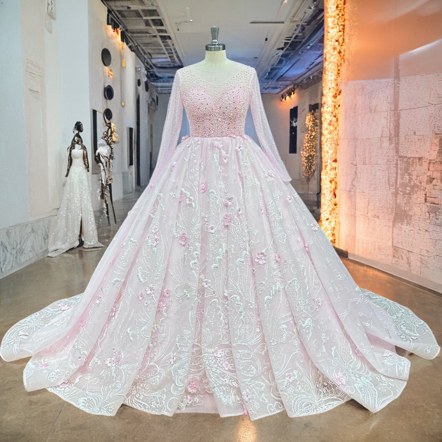 Pink long-sleeve princess wedding dress with white lace embroidery and crystal embellishments displayed on a mannequin in a bright showroom.