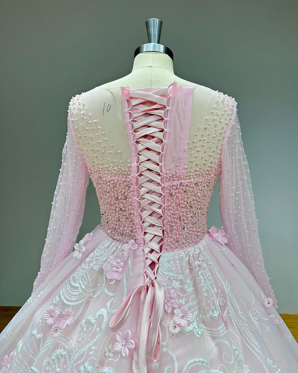Close-up back view of a pink modest wedding gown bodice highlighting a satin lace-up corset closure, sheer mesh paneling, and delicate scattered seed pearls.