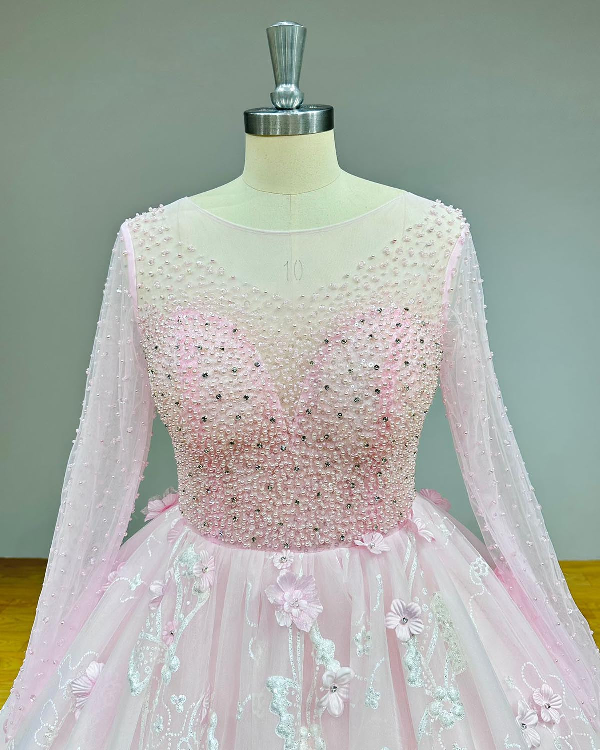 Macro view of a sweetheart neckline under a sheer high-neck overlay on a pink wedding gown, decorated with glittering crystals and beads on a mannequin.