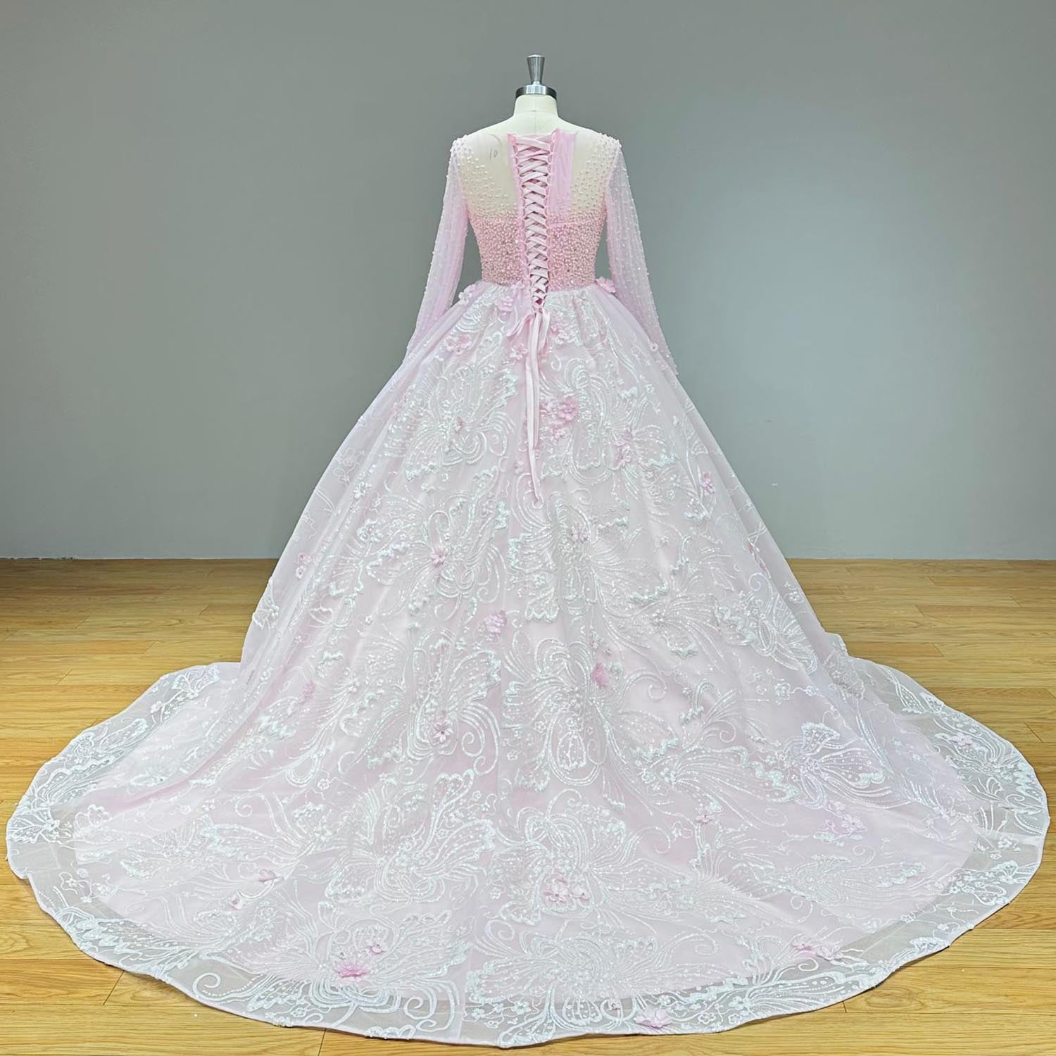 Full back view of a blush pink princess wedding dress on a mannequin, showcasing the expansive tulle and lace train decorated with handmade floral elements.