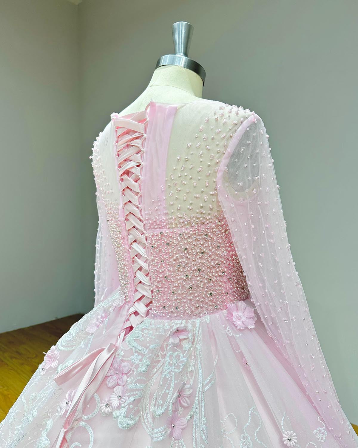 Three-quarter back perspective of a pink couture wedding dress showing the corset tie details and the premium beadwork cascading down the long sleeves.