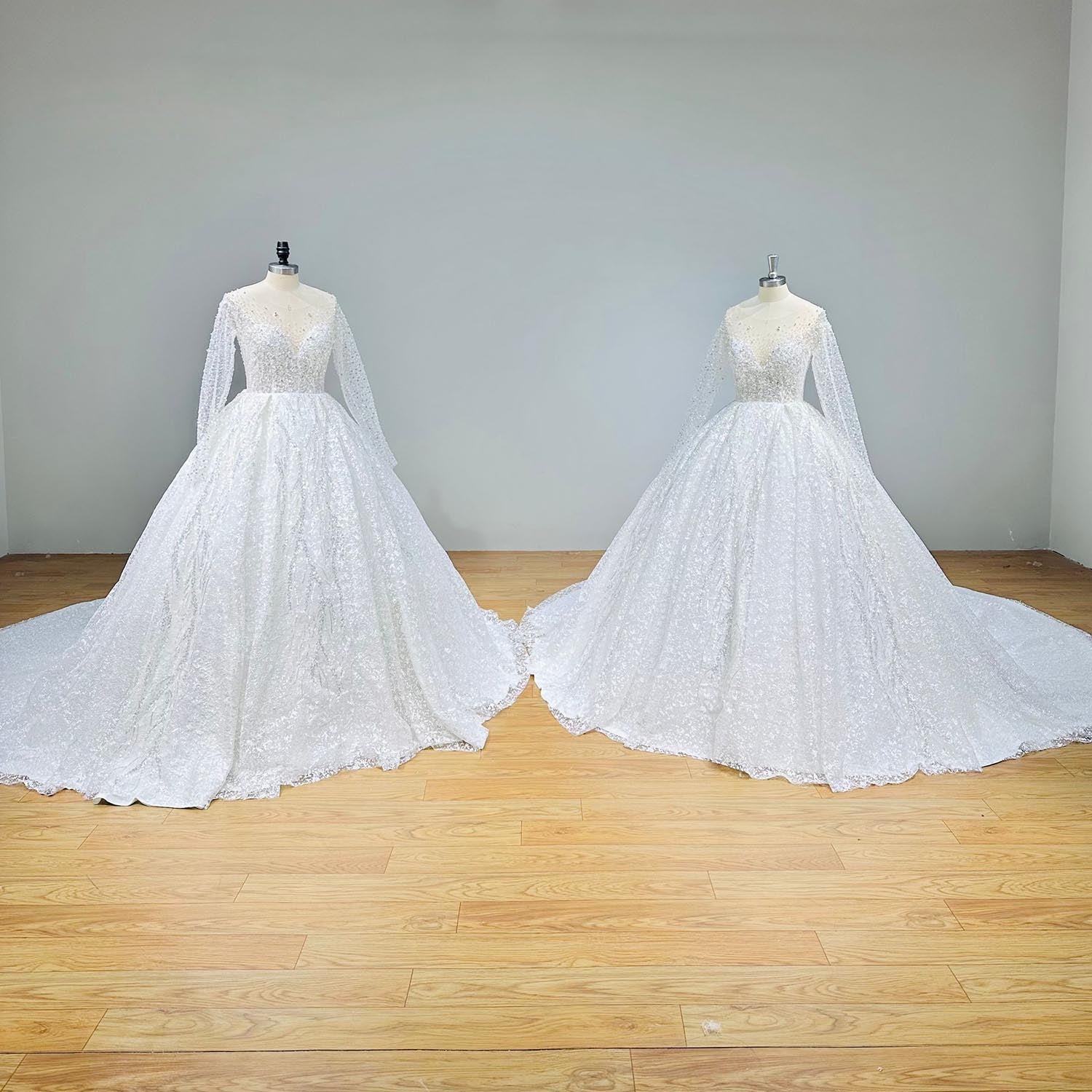 Two mannequins side-by-side in a bright studio space, both showcasing the radiant front view of a crystal beaded shining ball gown wedding dress with long sleeves.