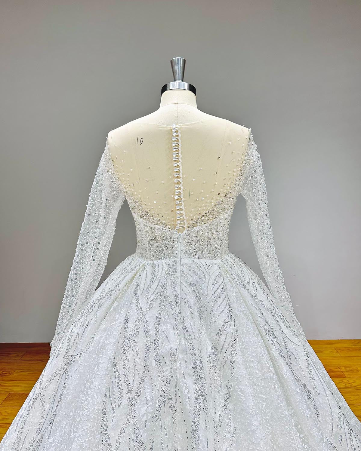 Close-up back bodice view of a luxury wedding gown on a mannequin, highlighting the elegant illusion back with a delicate button closure and crystal beaded long sleeves.