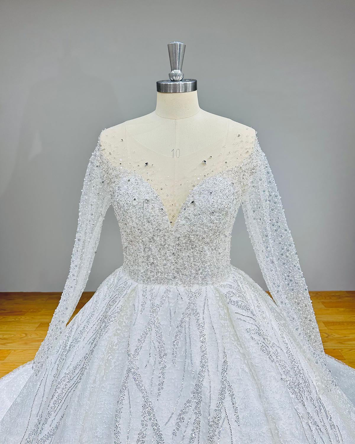 Close-up front bodice detail of a crystal beaded shining ball gown wedding dress on a mannequin, emphasizing the sheer illusion V-neckline and heavy sparkling embellishments.
