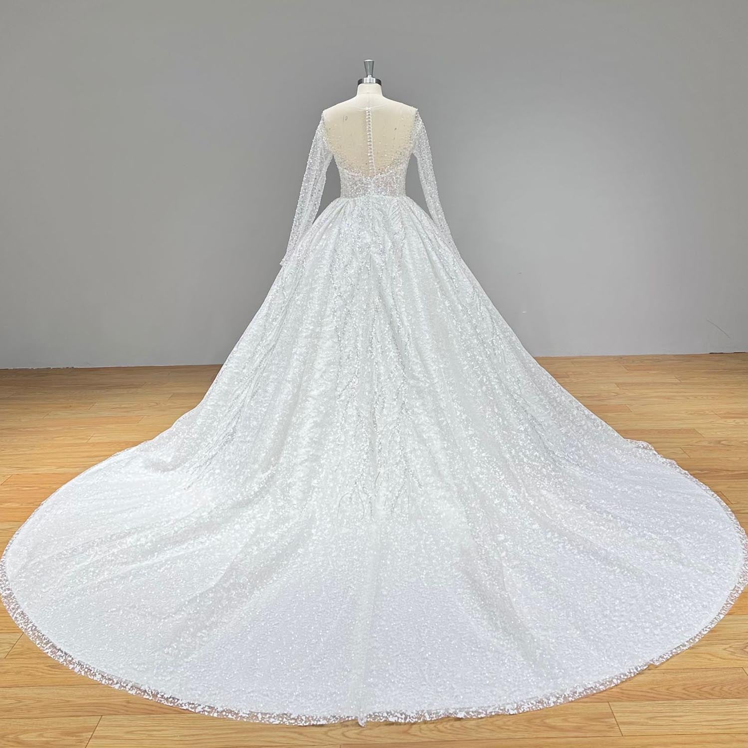 Dramatic full back view of a shining ball gown wedding dress on a mannequin, perfectly capturing the delicate illusion back, sheer long sleeves, and a sweeping, fully beaded circular train.