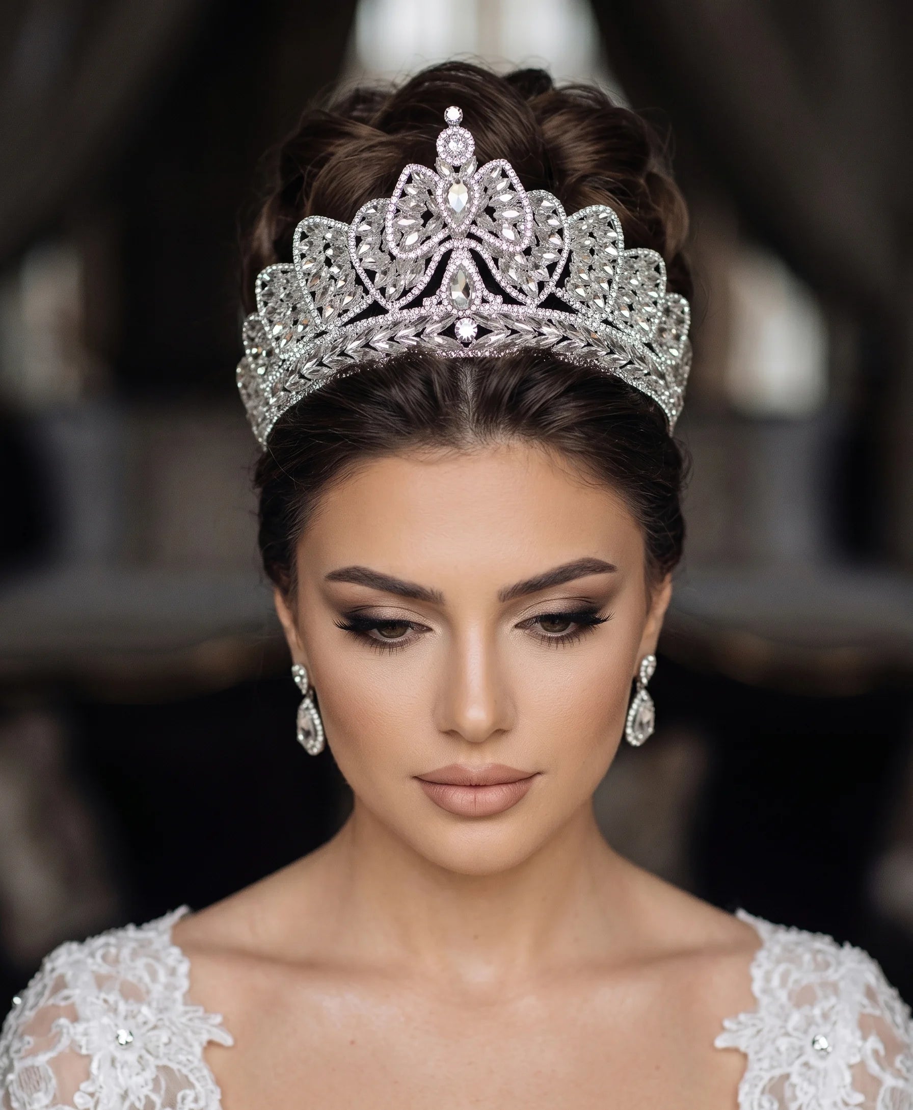A bride looking down while wearing a silver rhinestone wedding headpiece designed as a crystal bowknot bridal crown tiara.