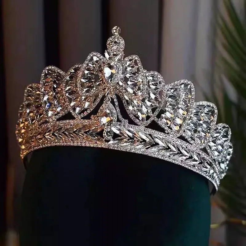 A silver rhinestone wedding headpiece crafted into an intricate crystal bowknot tiara, displayed on a dark green mannequin head.